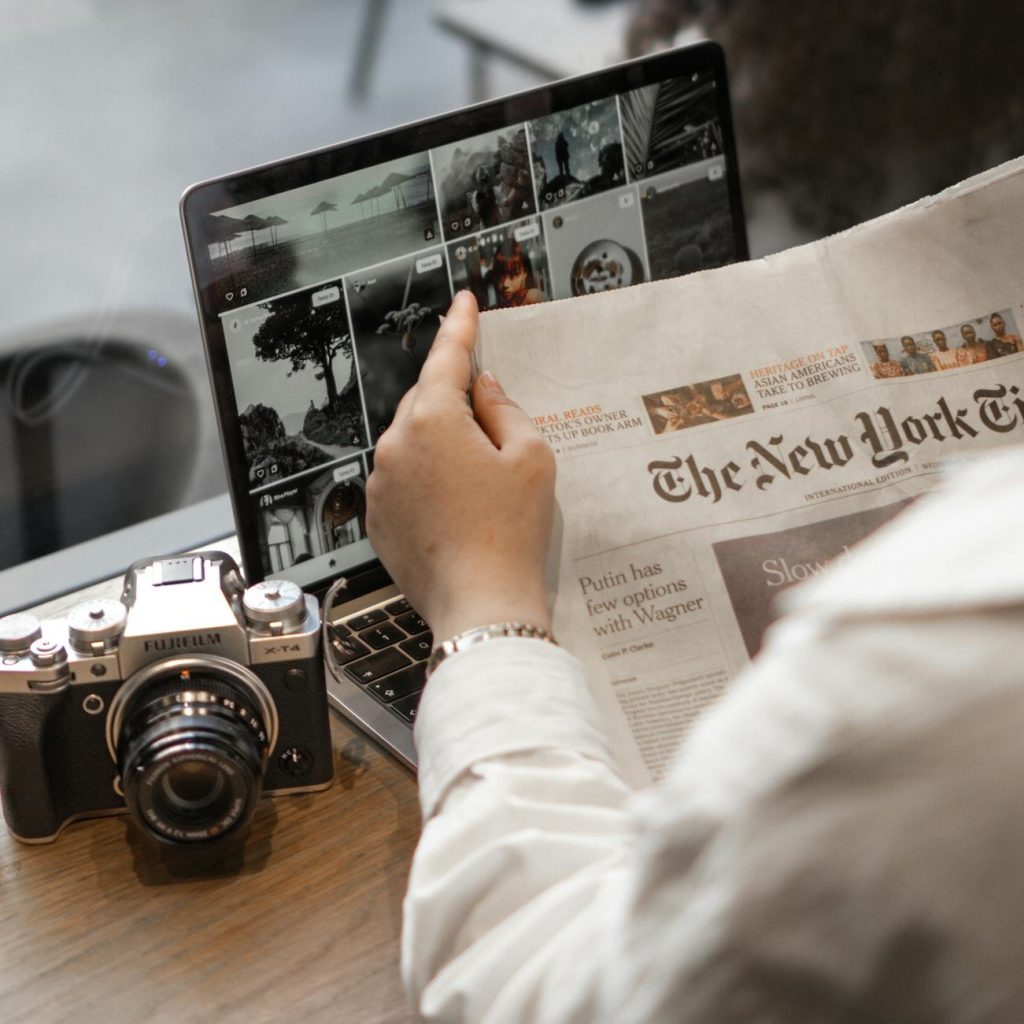 hand holding new york times near camera and laptop