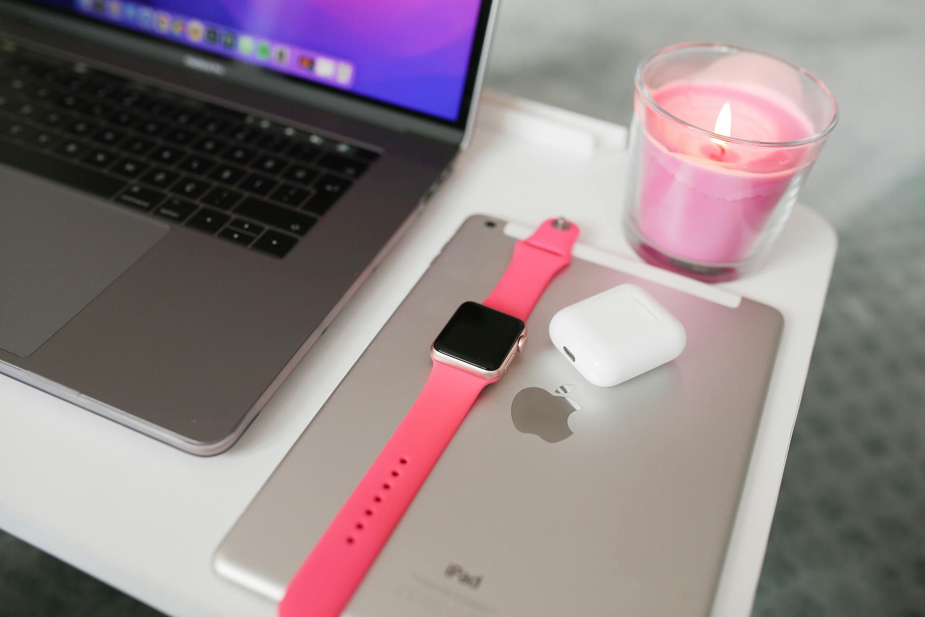 a pink smart watch beside airpod case on gray ipad